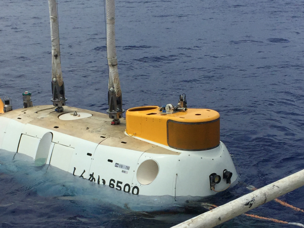 写真：海上に浮かぶ「しんかい6500」。白い船体と黄色い上部ハッチが特徴的